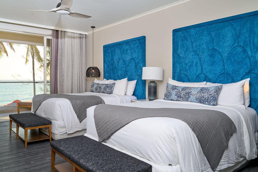 Two beds with blue headboards in a room overlooking the ocean.