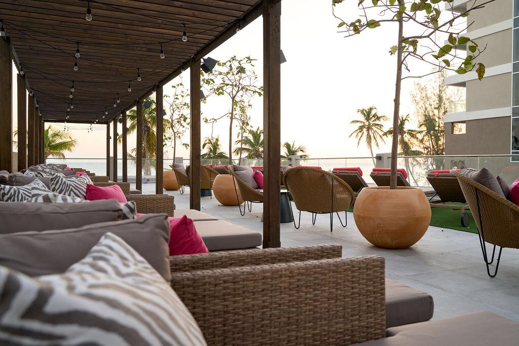 :Beach club at luxury hotel with palm trees, lounge chairs, and umbrellas on sandy beach.
